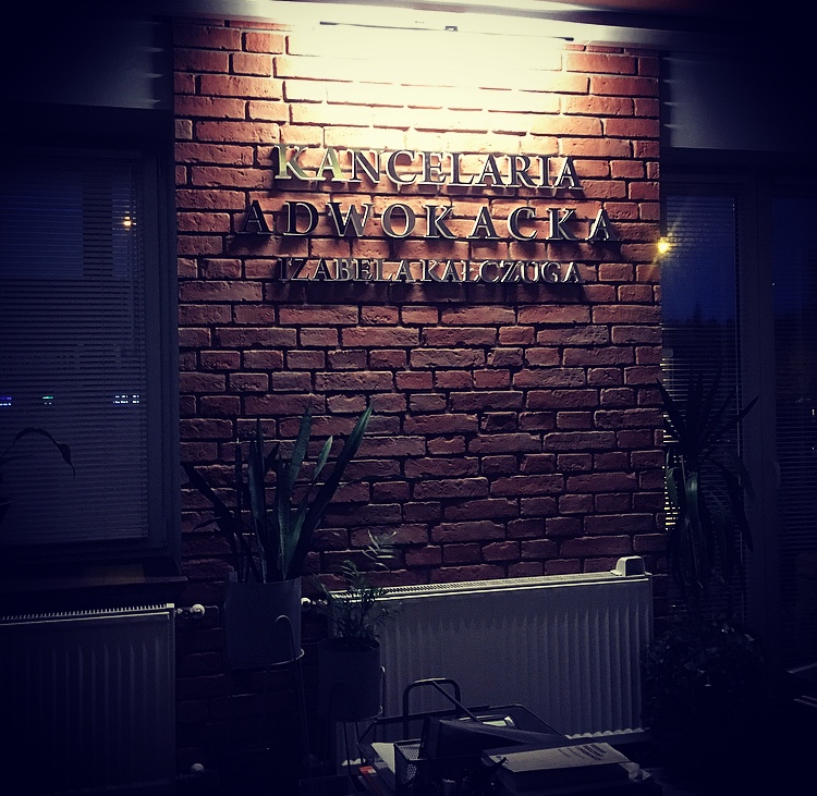Szyld Kancelarii Adwokackiej Izabela Kałczuga na ścianie z cegły